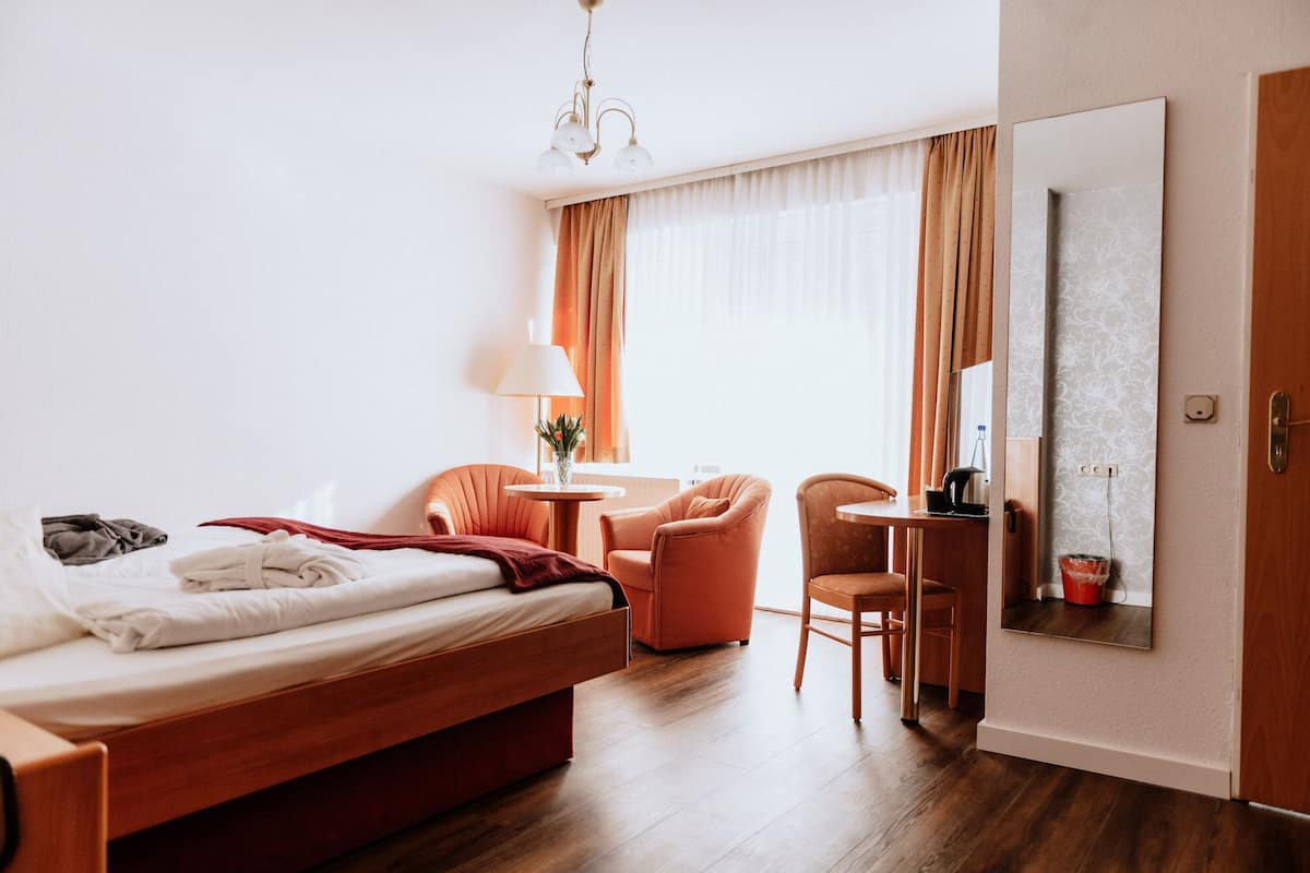 A hotel room with a bed, a desk, a chair, a lamp, and a large mirror on the wall.