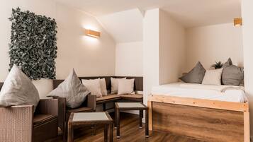 Une chambre moderne comprenant un lit, un canapé, deux fauteuils, une petite table et une plante fixée au mur.