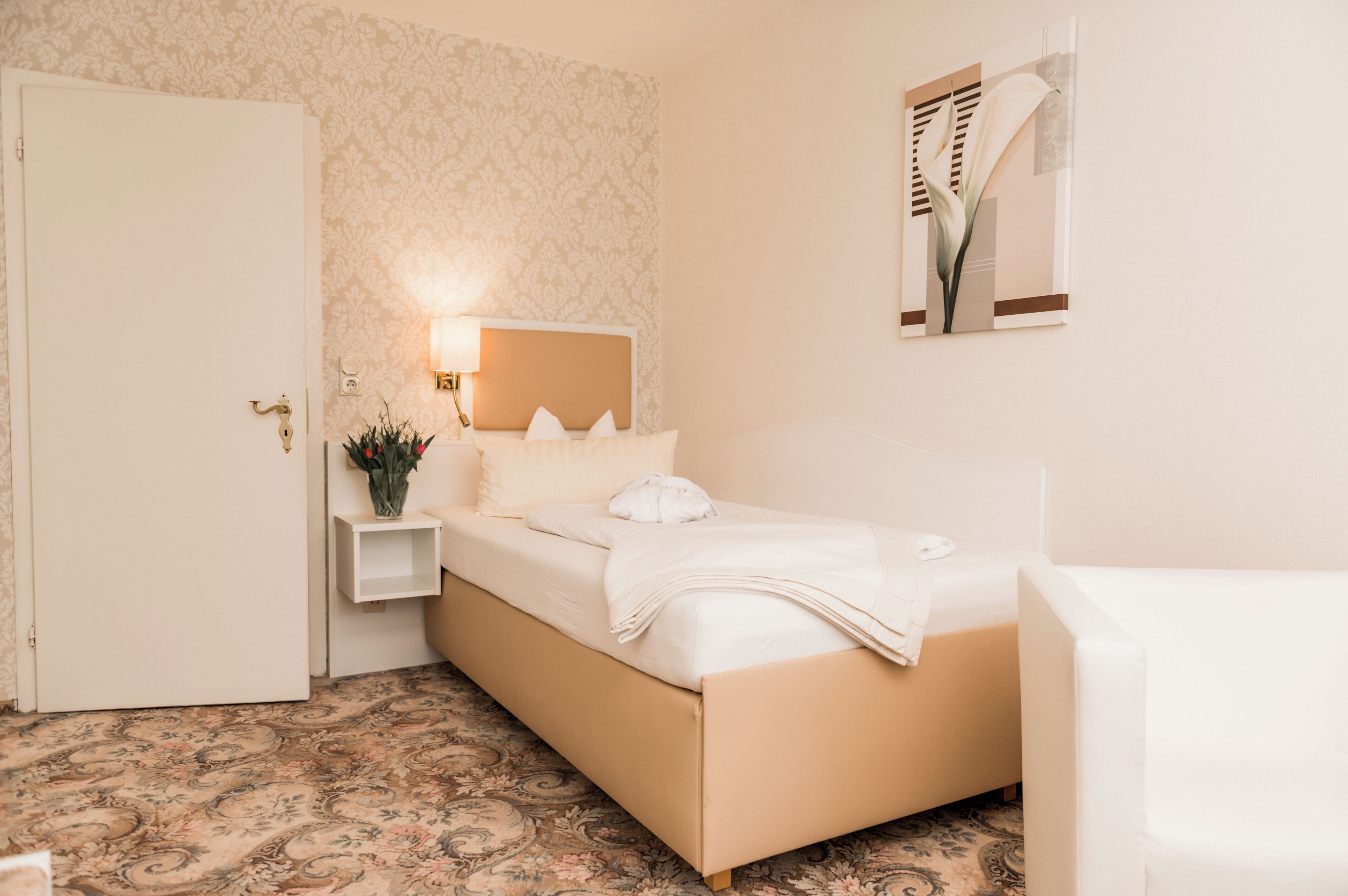Ein Schlafzimmer mit Bett, Nachttisch, Lampe und einem Spiegel an der Wand.