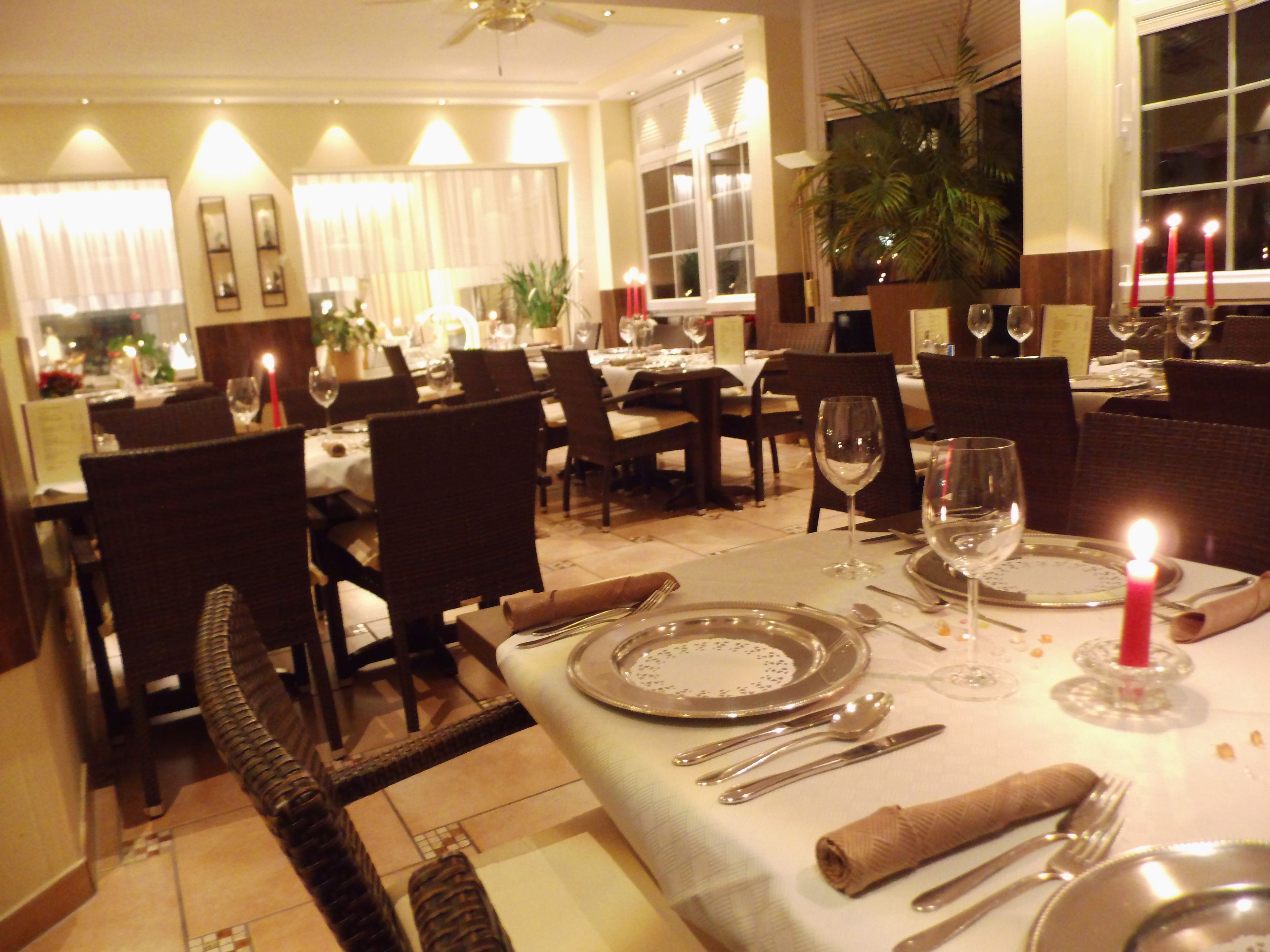 A well-lit dining area with tables set for a meal, featuring chairs, plates, cutlery, and candles.