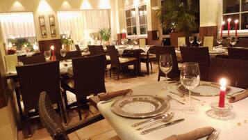 A well-lit dining area with tables set for a meal, featuring chairs, plates, cutlery, and candles.