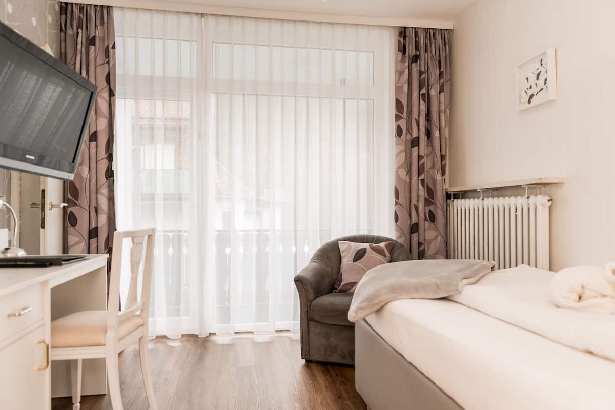 A bedroom with a bed, a desk with a computer, a chair, and a radiator.