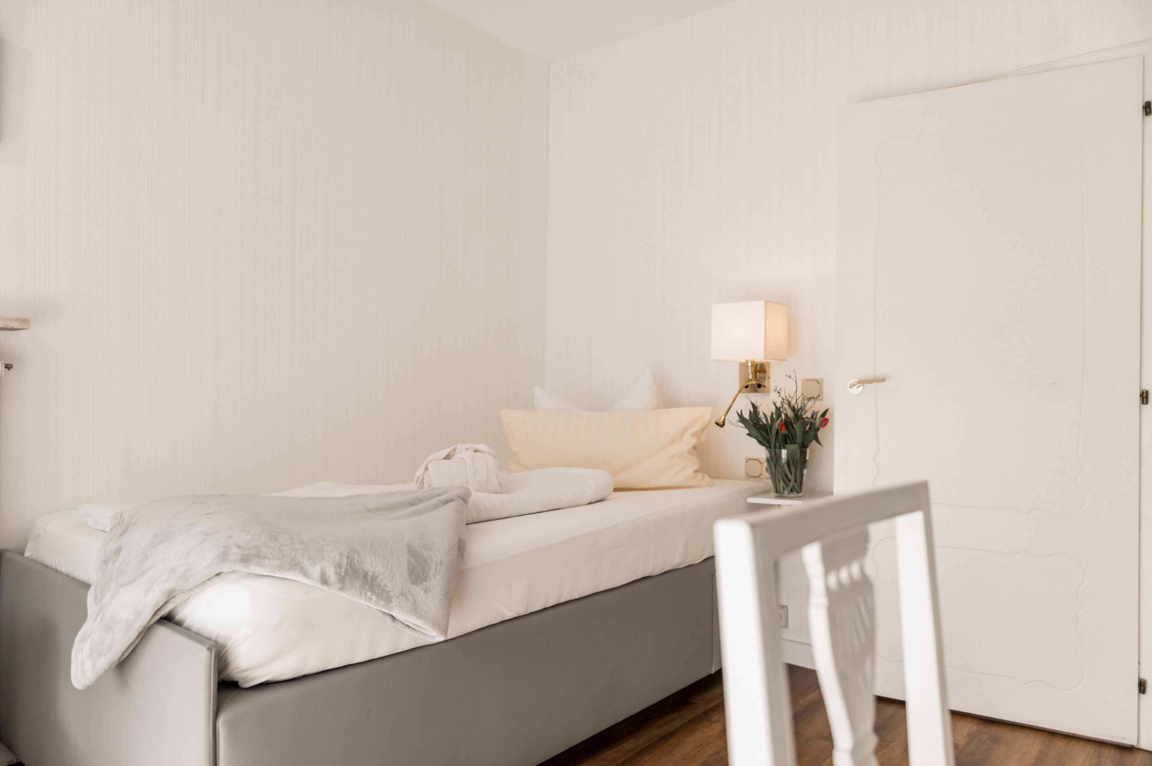 A minimalist bedroom with a bed, bedside table, lamp, and a small plant.