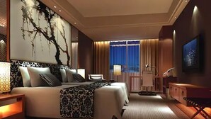 A modern hotel room with a large bed, a desk, and a chair. There is a window with curtains and a painting on the wall. - Mövenpick Enshi (Enshi)