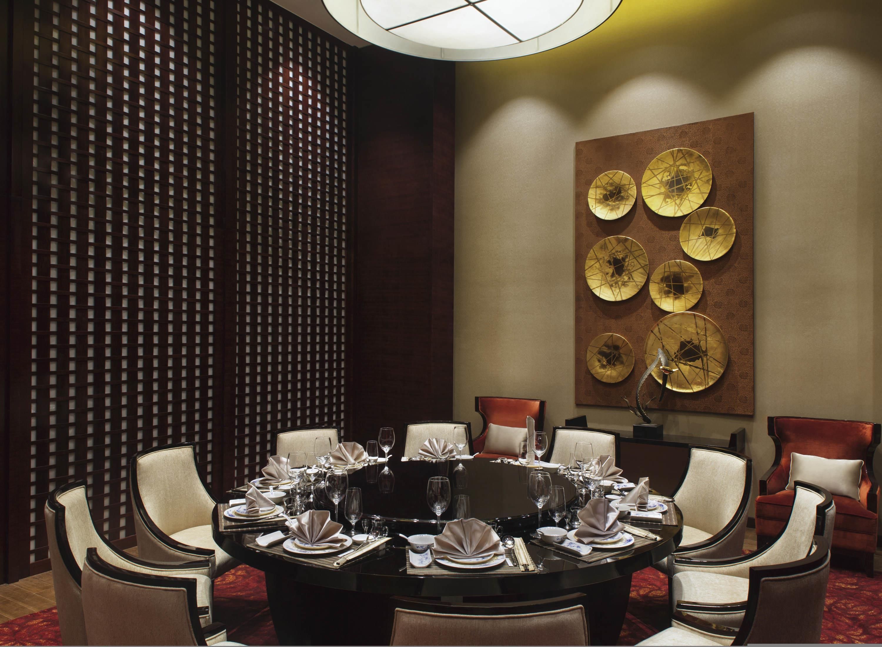 Une salle à manger avec une table ronde dressée pour six personnes, entourée de six chaises, agrémentée d’un élément décoratif mural et d’un papier peint à motifs.