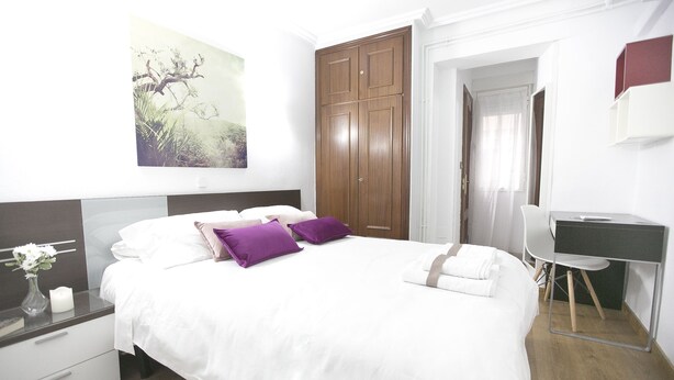 A neatly arranged bedroom with a bed, bedside table, and a desk.