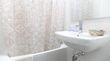 Een badkamer met een witte wasbak, een spiegel en een douchegordijn met een geometrisch patroon.