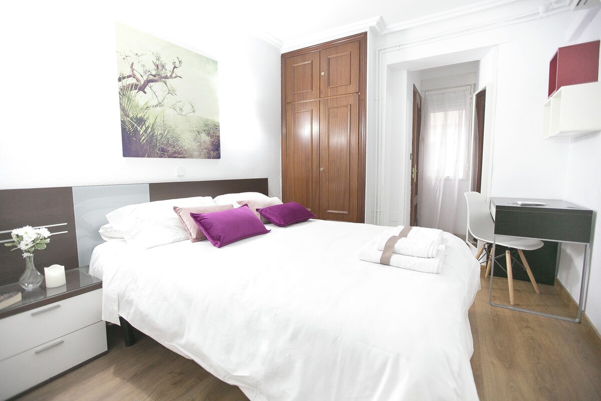 Un dormitorio ordenado con cama, mesita de noche y escritorio.