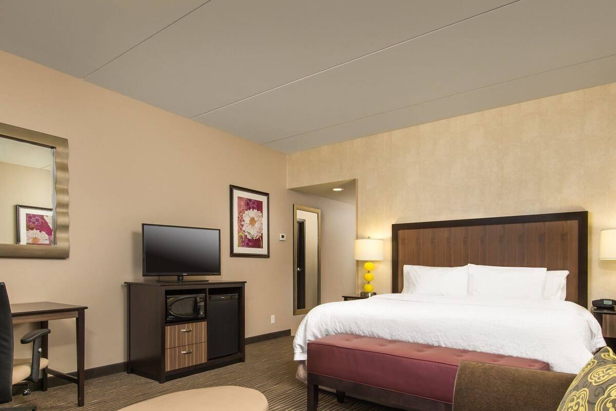 A hotel room with a bed, a desk, a television, and a mirror.
