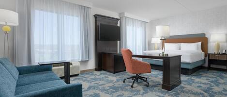 A hotel room with a bed, a desk, a chair, a TV, and a lamp.