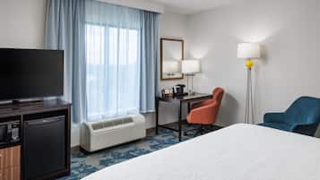 A hotel room with a bed, a desk, a chair, a television, a lamp, and a heater.
