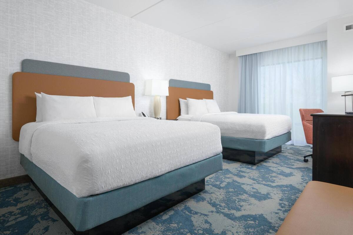 Two beds with white linens, a desk, and a chair in a hotel room.