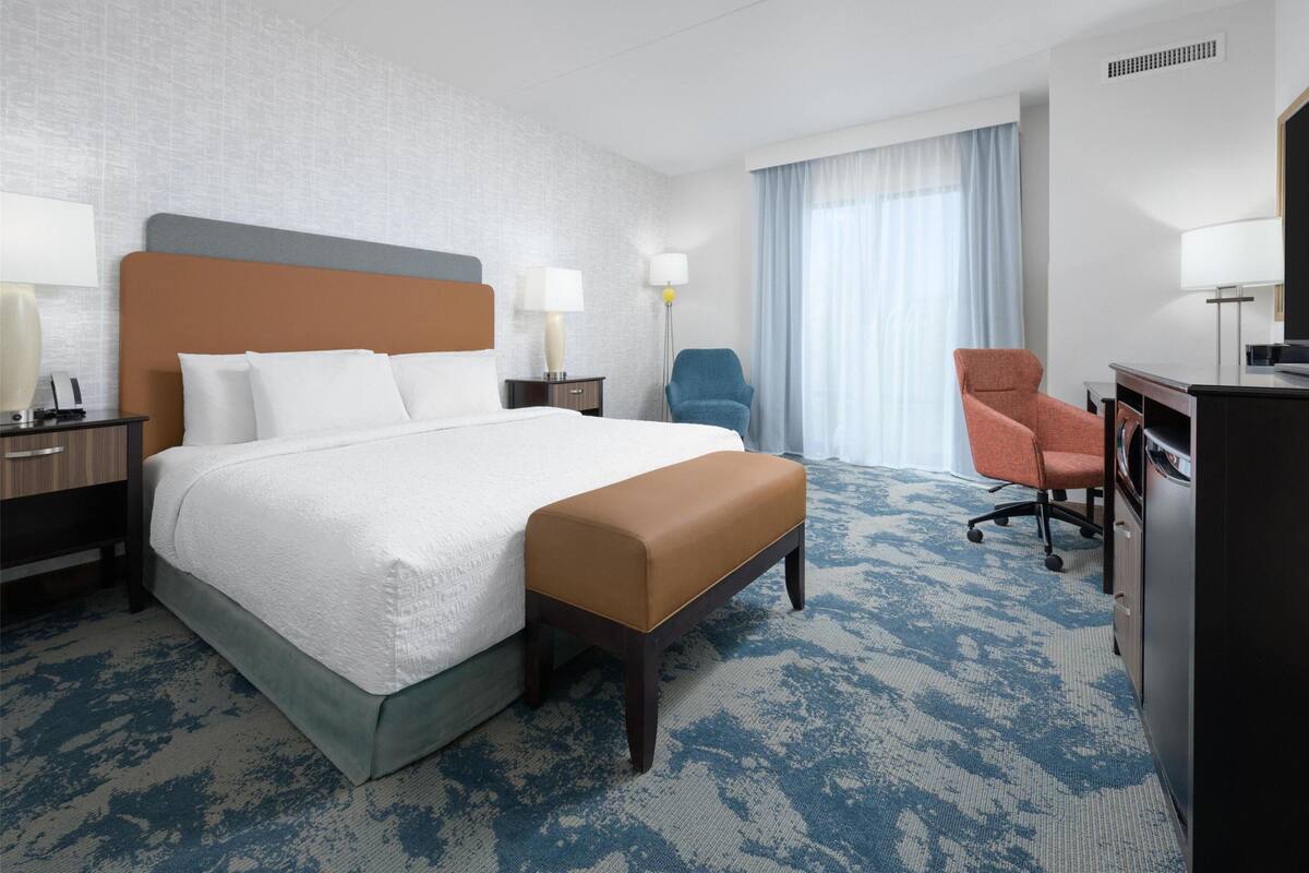 A hotel room with a large bed, a desk, two chairs, and a television.