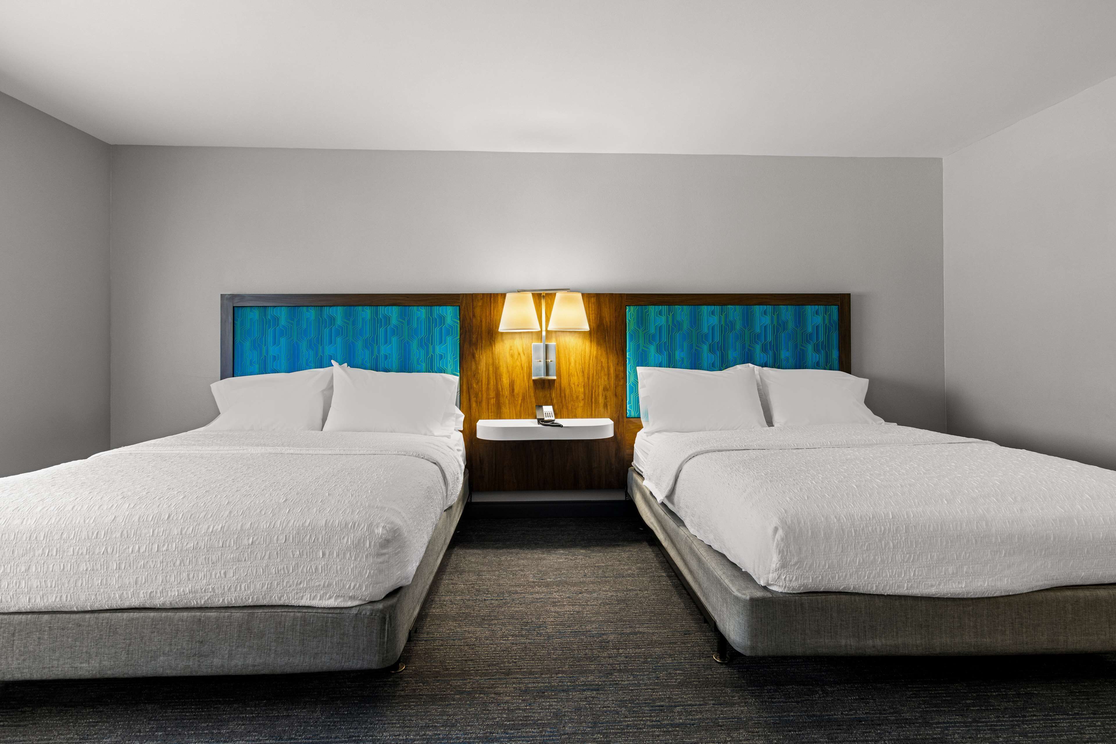 Ein Hotelzimmer mit zwei Einzelbetten, einem Holz-Kopfteil, einem Nachttisch mit Lampe und einem kleinen Waschbecken.