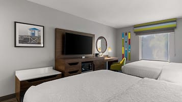 A hotel room with two beds, a TV, a desk with a mirror, a framed picture on the wall, and a window with a view.