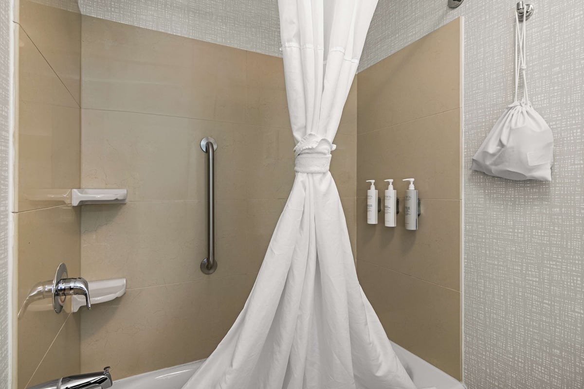 A shower with a white curtain, a grab bar, and toiletries on the wall.