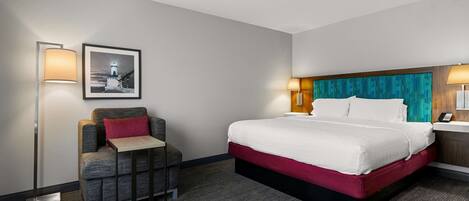 A hotel room with a bed, a chair, a desk, and a lamp.