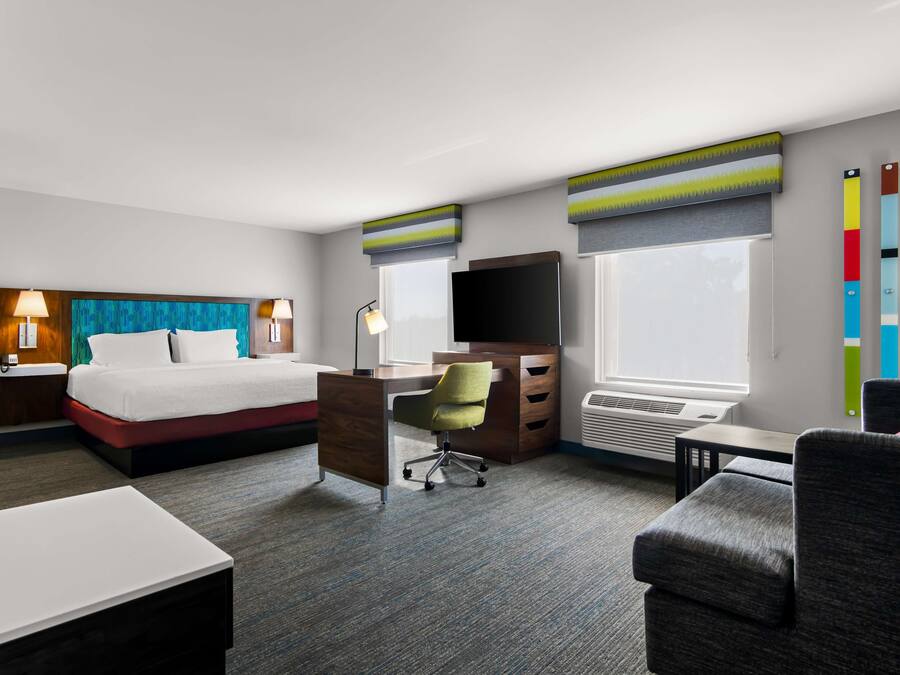 Ein Hotelzimmer mit Bett, Schreibtisch, Stuhl, Fernseher und Klimaanlage.