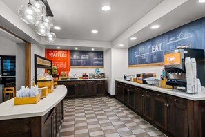 A modern cafe with a checkered floor, a counter with various food items, and a wall with chalkboard-style menu boards.