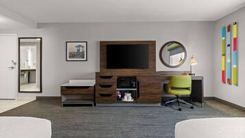 A hotel room with a bed, a desk with a TV, a microwave, a chair, and a mirror.