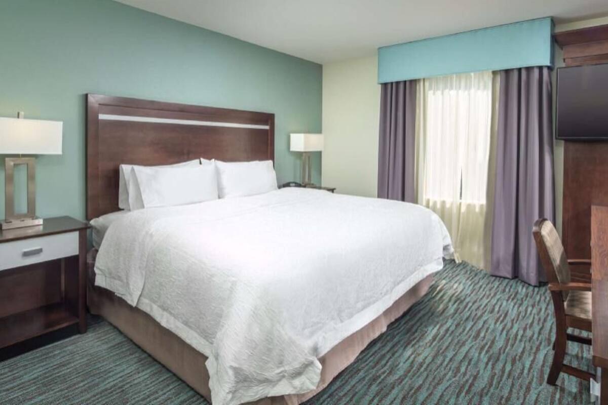 A hotel room with a large bed, a desk, a television, and a window with curtains.
