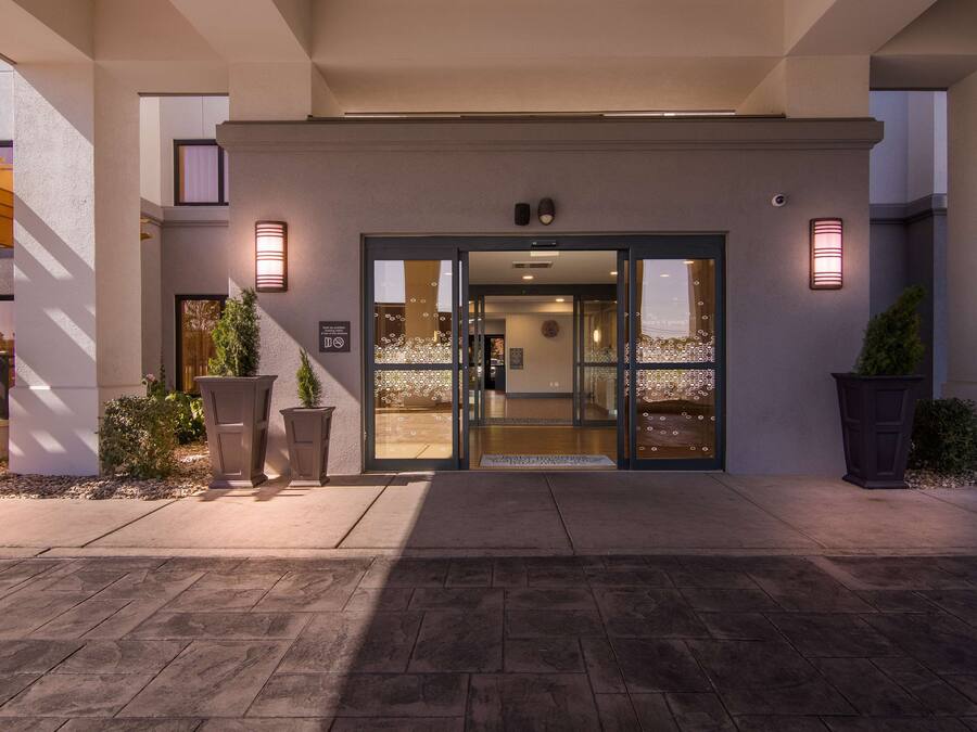 A hotel entrance with a modern design, featuring a glass door and a welcoming outdoor area with potted plants.