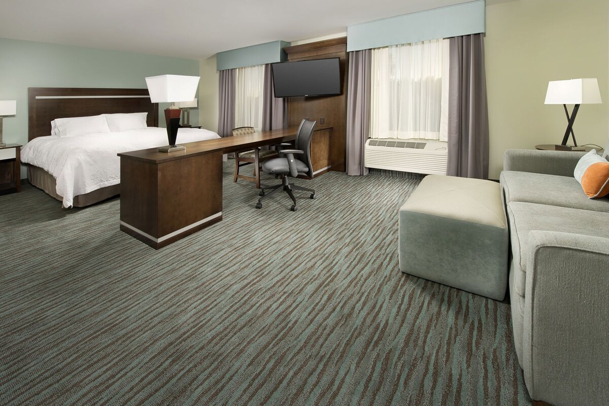 A hotel room with a bed, desk, chair, TV, air conditioning unit, and a couch.