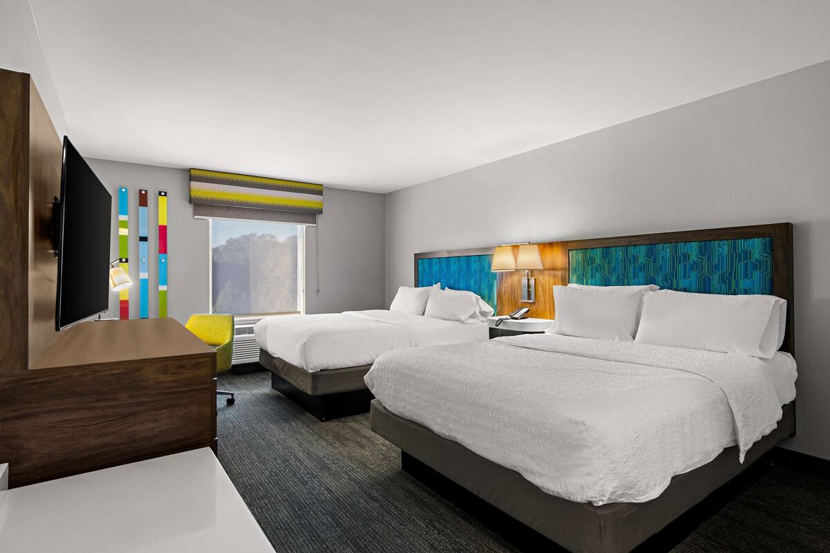 A hotel room with two beds, a desk, a TV, and a window with a view.