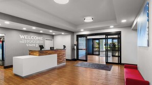 A reception area with a wooden floor, a reception desk, a red bench, and a glass door leading outside. - Hampton Inn & Suites Schererville (Schererville)