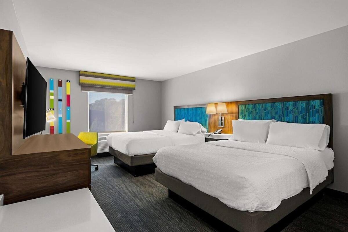 A hotel room with two beds, a desk, a TV, and a window with a view.