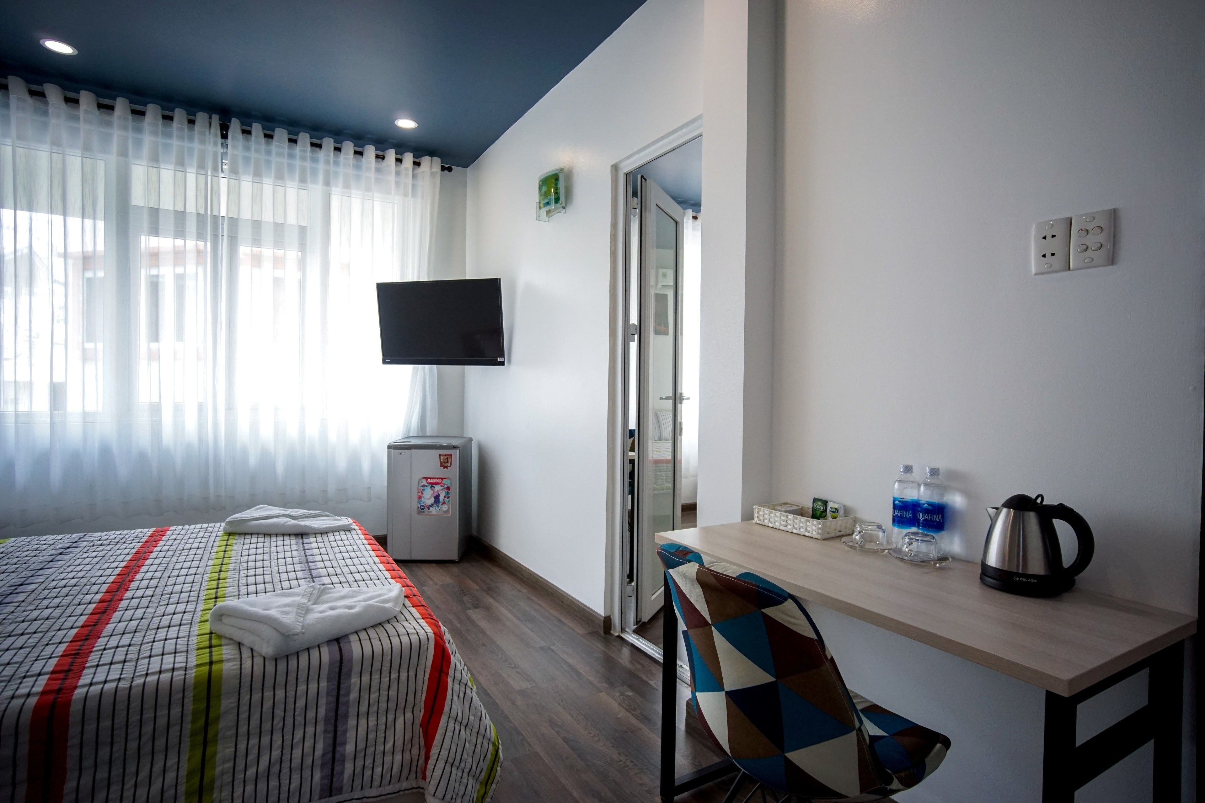 Une chambre d’hôtel comprenant un lit, un bureau avec une chaise, une télévision, un réfrigérateur et une porte donnant sur une autre pièce.