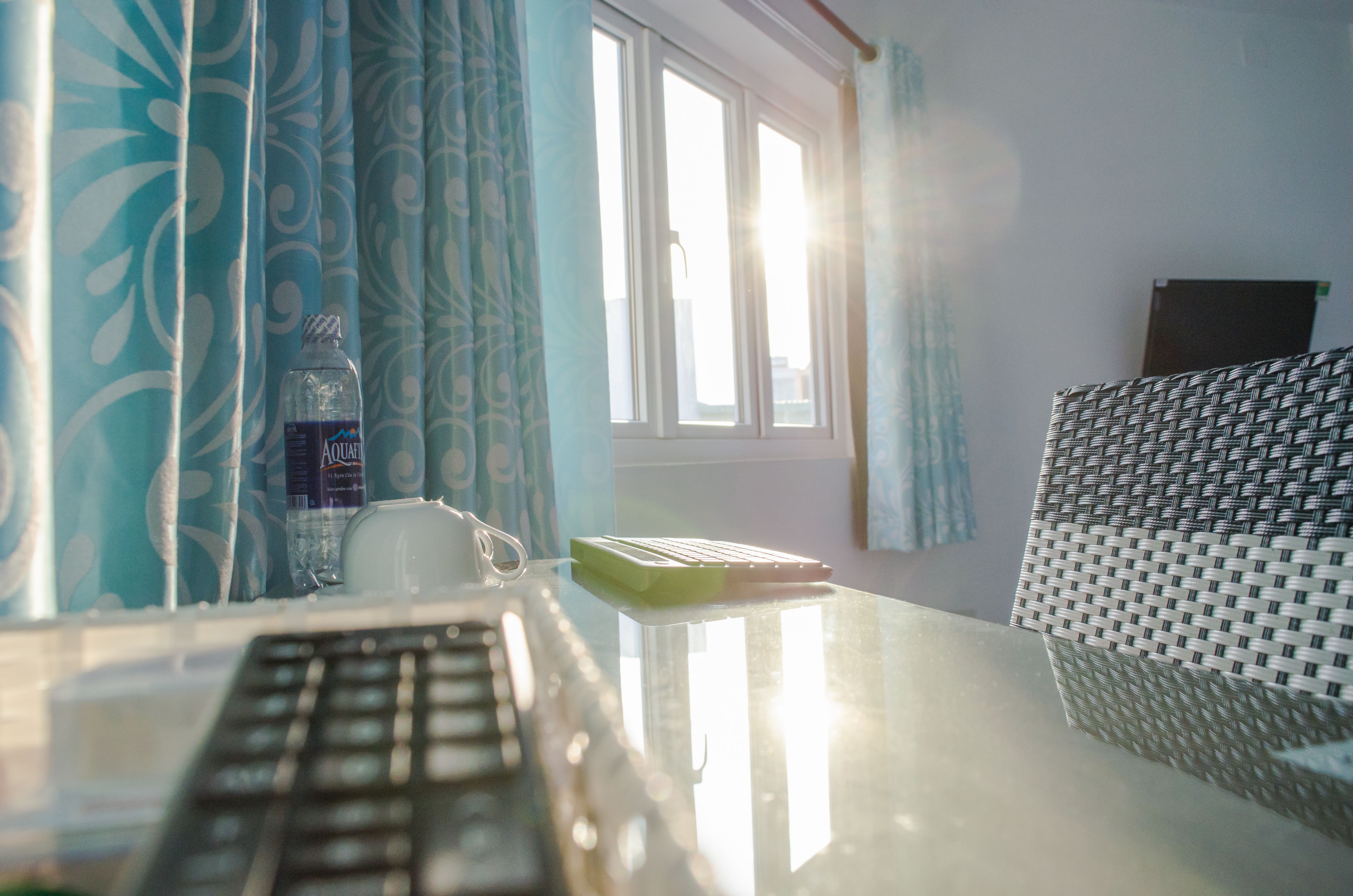 A room with a desk, a keyboard, a water bottle, a cup, and a woven chair.