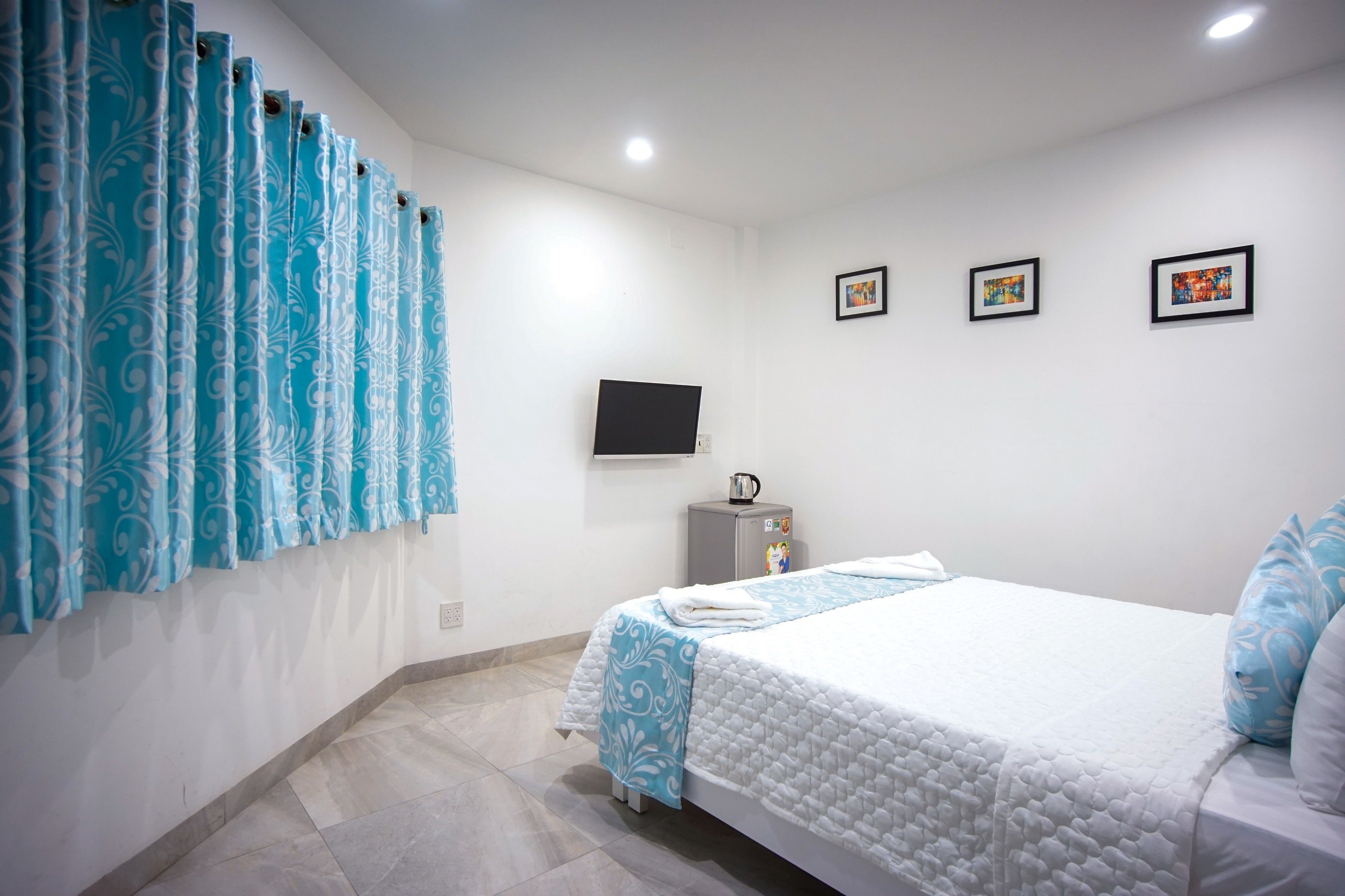 A bedroom with a bed, a TV, a small cabinet, and a window with curtains.