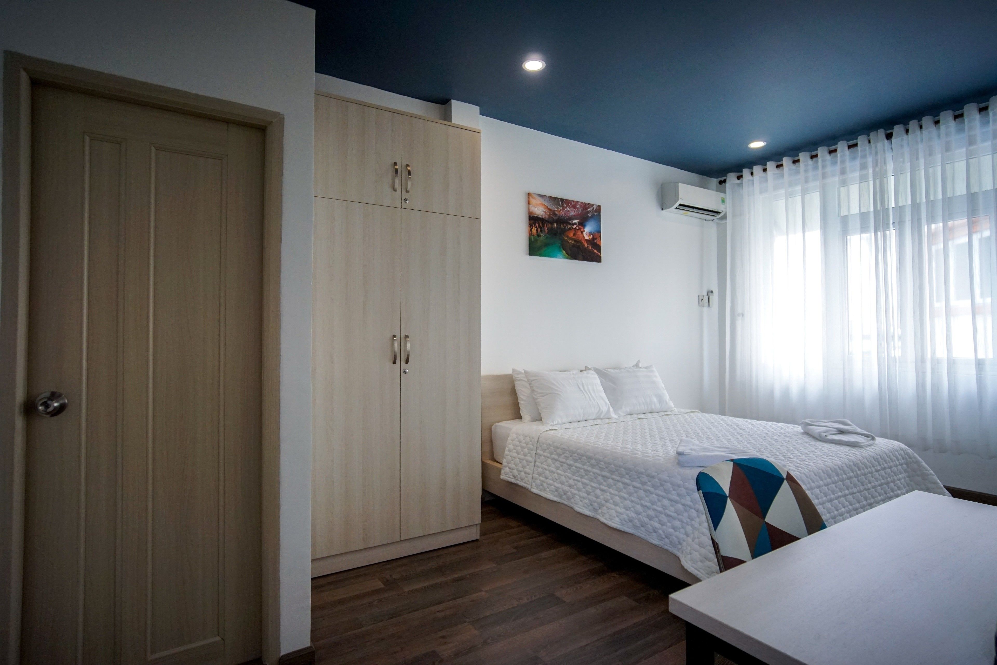 A bedroom with a bed, a wardrobe, a table, and a painting on the wall.