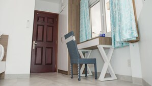 A room with a wooden door, a white desk with a chair, and a window with curtains. - LeBlanc Saigon (Ho Chi Minh City)