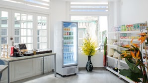 A bright, well-lit room with a refrigerator stocked with beverages, a coffee station, and a shelf with various items. - LeBlanc Saigon (Ho Chi Minh City)