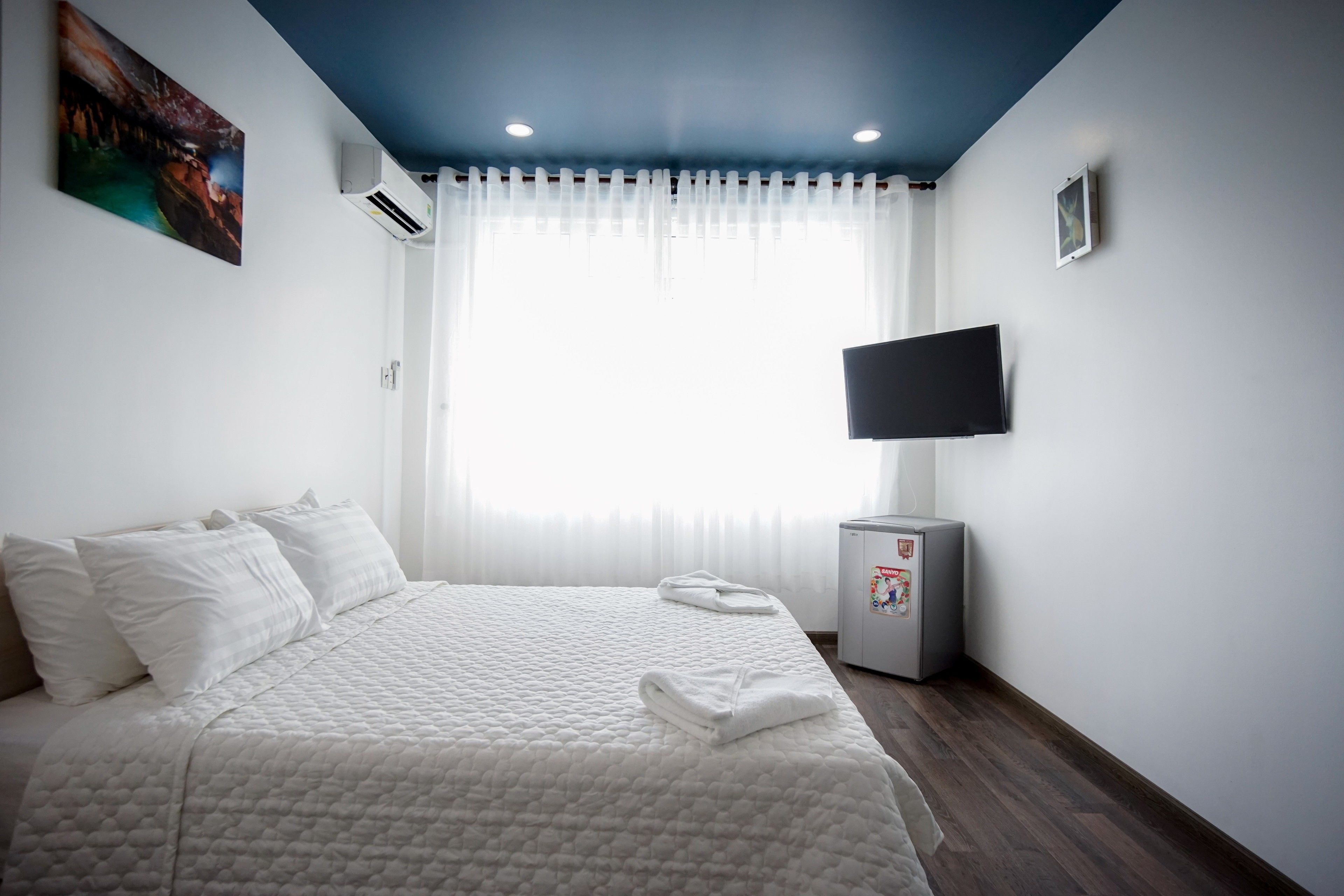 Quarto de hotel com cama grande, televisão de tela plana na parede e janela com cortinas leves.