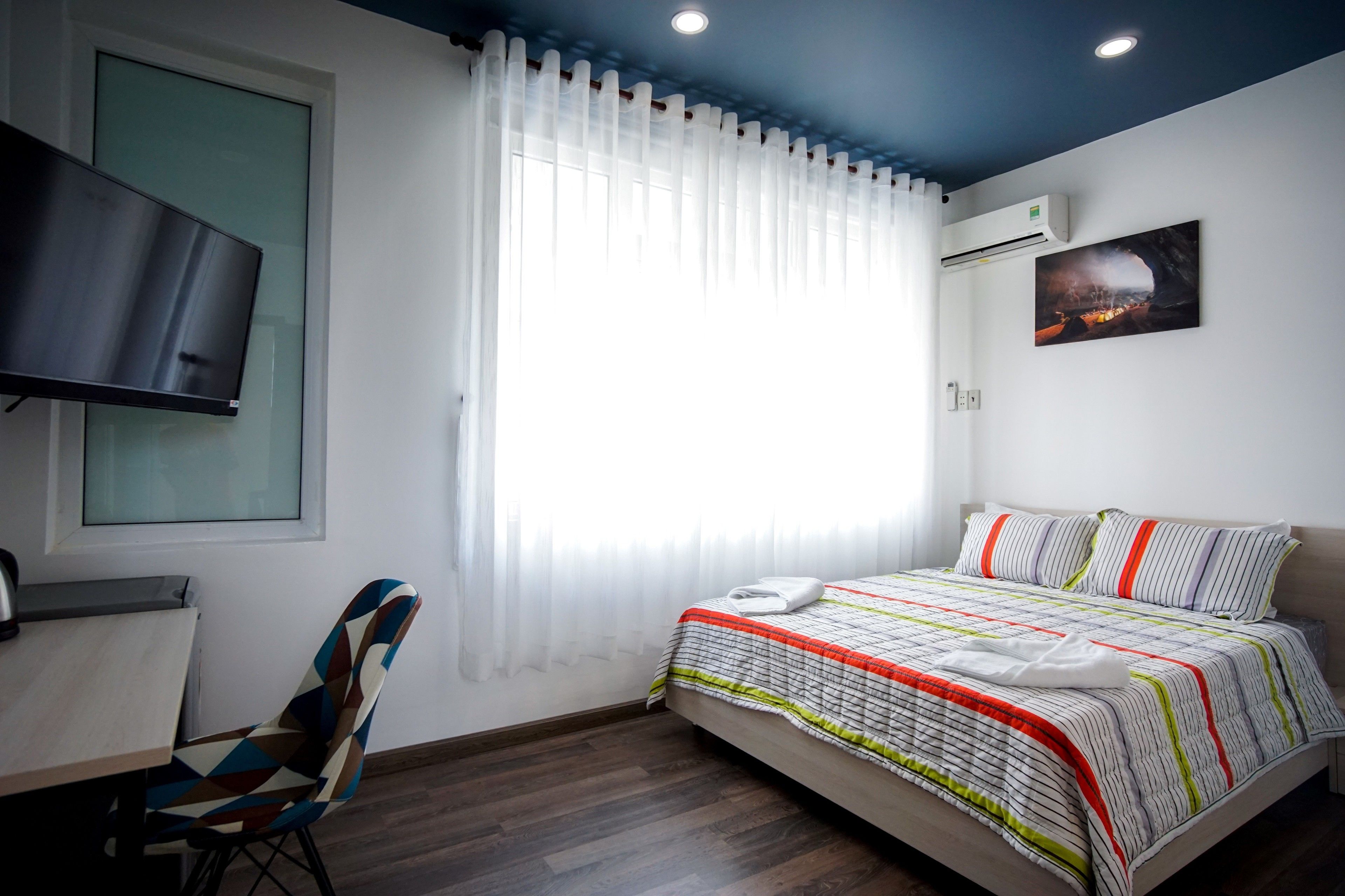 Une chambre d’hôtel équipée d’un lit, d’un téléviseur fixé au mur, d’une fenêtre avec des rideaux légers et d’un appareil de climatisation.