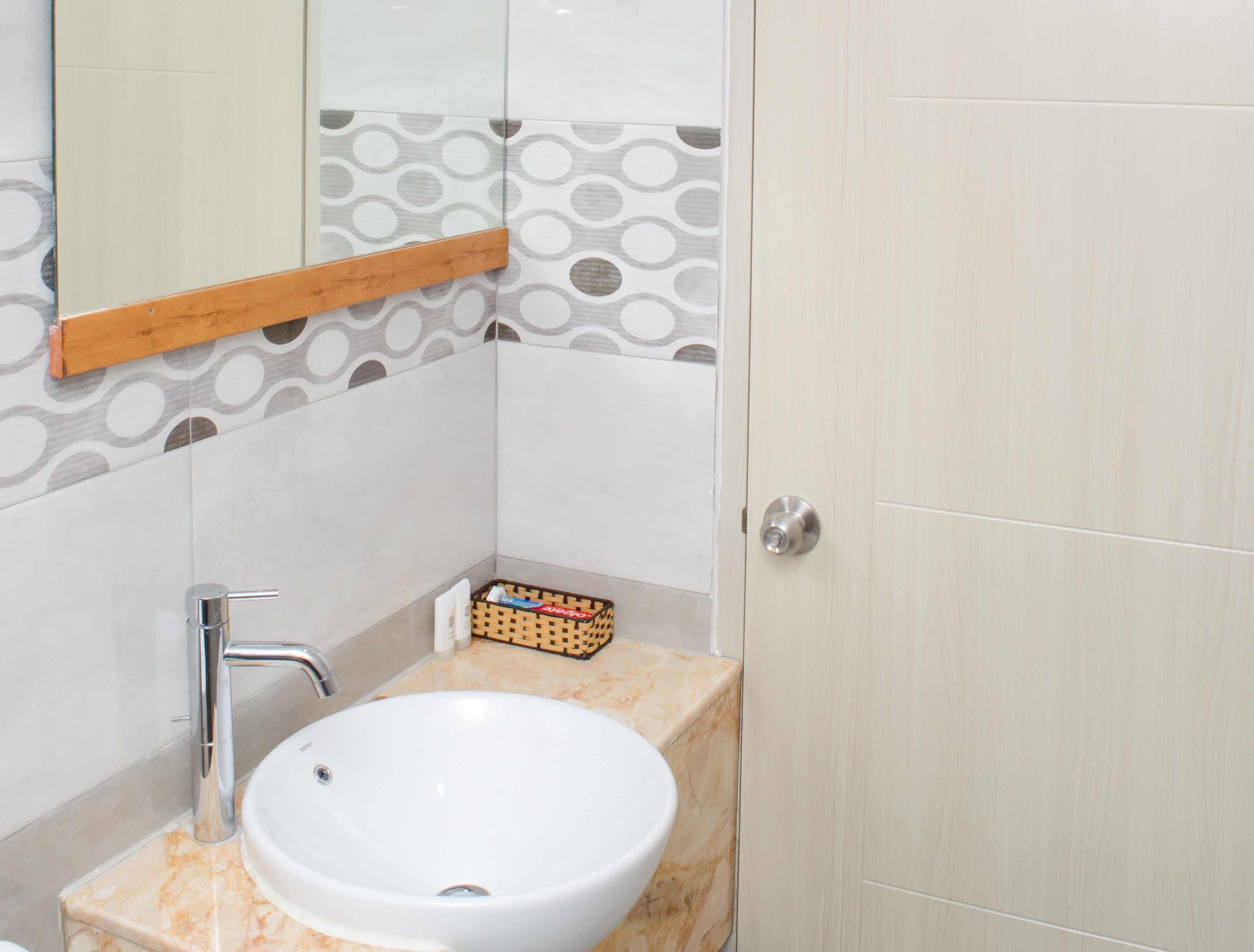 A bathroom with a white sink, a wooden-framed mirror, and patterned tiles on the walls.