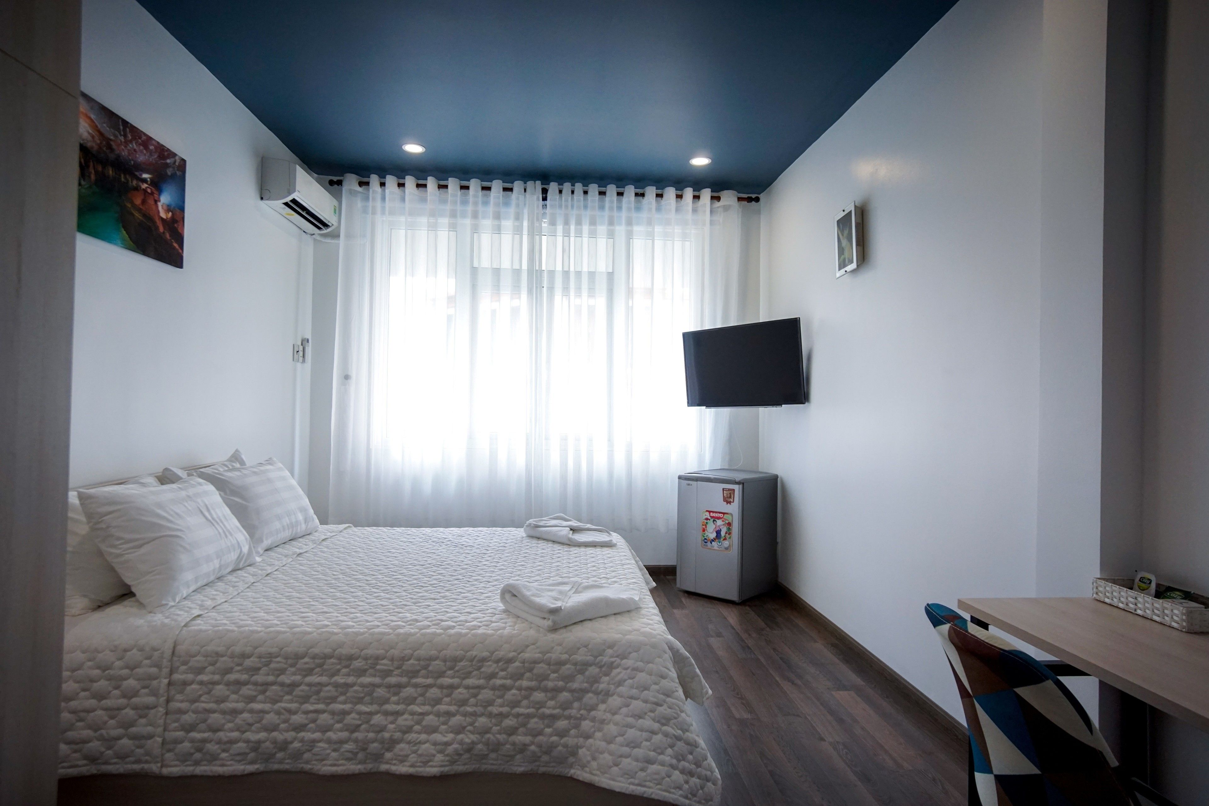 Une chambre à coucher avec un lit, un bureau, une télévision et un réfrigérateur.
