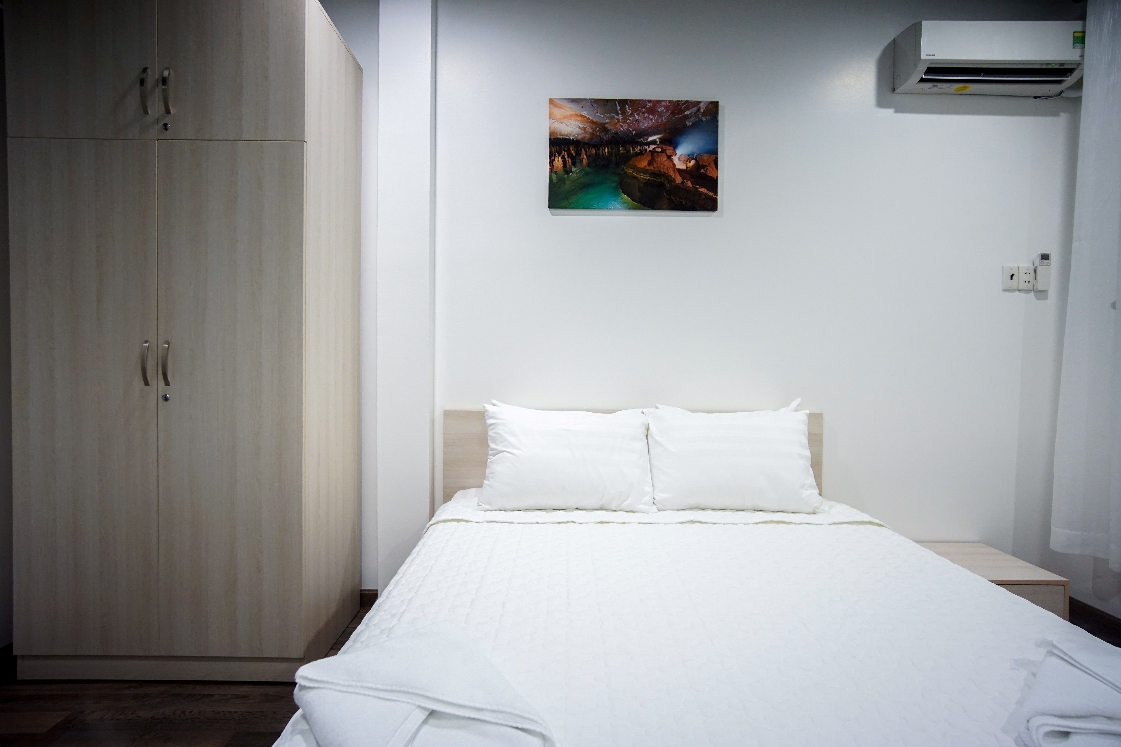 Una camera d'albergo con un letto, un armadio, un quadro appeso al muro e un condizionatore d'aria.