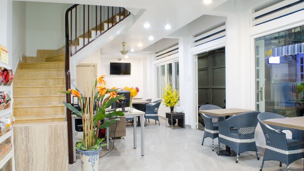 A modern interior with a staircase, a dining area with wicker furniture, and a potted plant. - LeBlanc Saigon (Ho Chi Minh City)