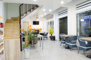 A modern interior with a staircase, a dining area with wicker furniture, and a potted plant. - LeBlanc Saigon (Ho Chi Minh City)