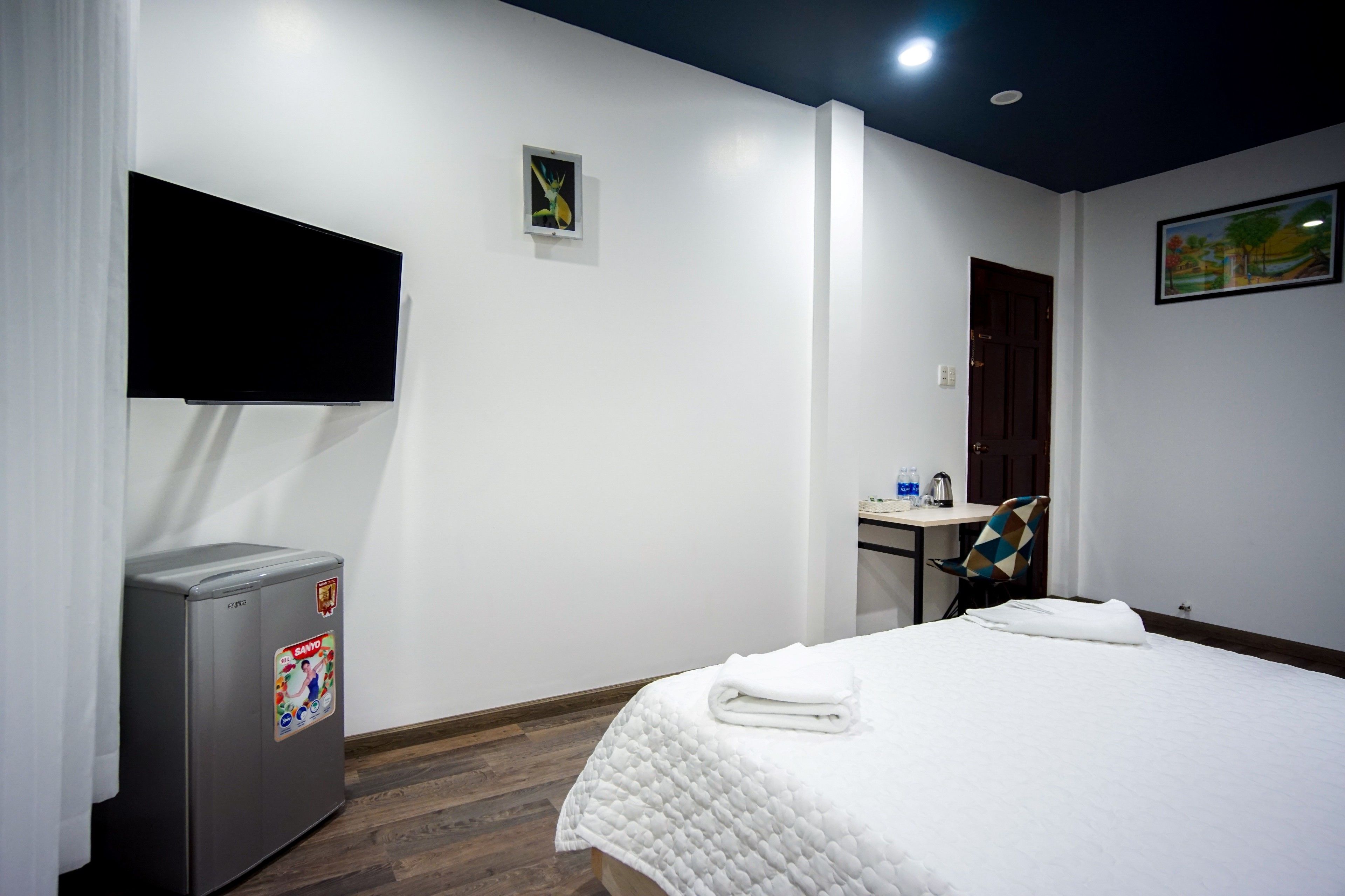 Una habitación de hotel con cama, escritorio, silla, televisor y refrigerador.