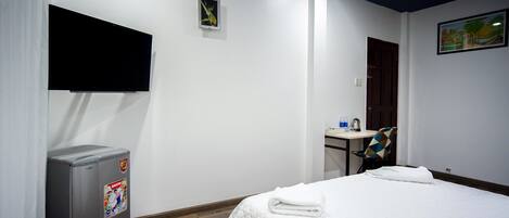Una habitación de hotel con cama, escritorio, silla, televisor y refrigerador.