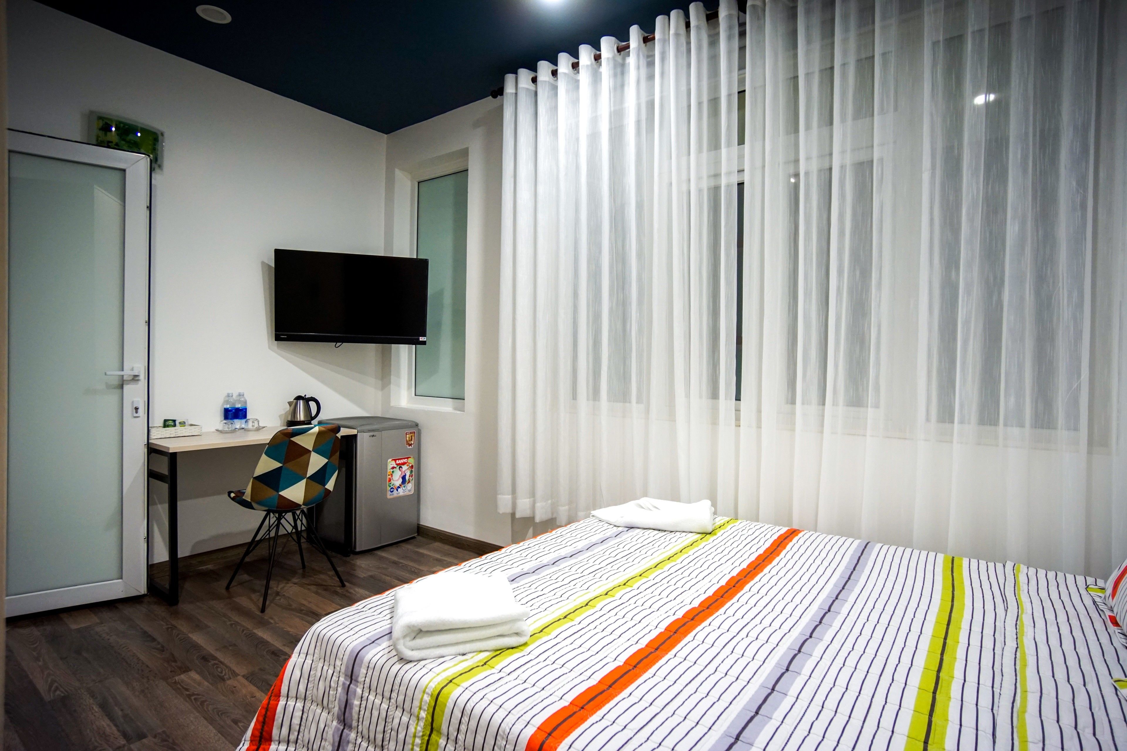 A hotel room with a bed, a desk, a chair, a television, and a window with curtains.