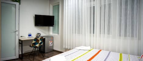 A hotel room with a bed, a desk, a chair, a television, and a window with curtains.