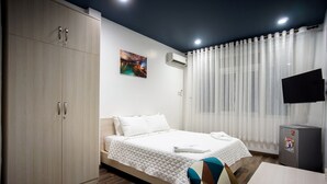 A hotel room with a bed, a wardrobe, a TV, and a small refrigerator. - LeBlanc Saigon (Ho Chi Minh City)