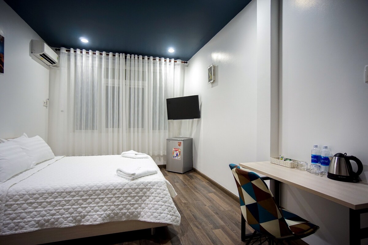 Una habitación de hotel con cama, escritorio, silla, televisor y refrigerador.