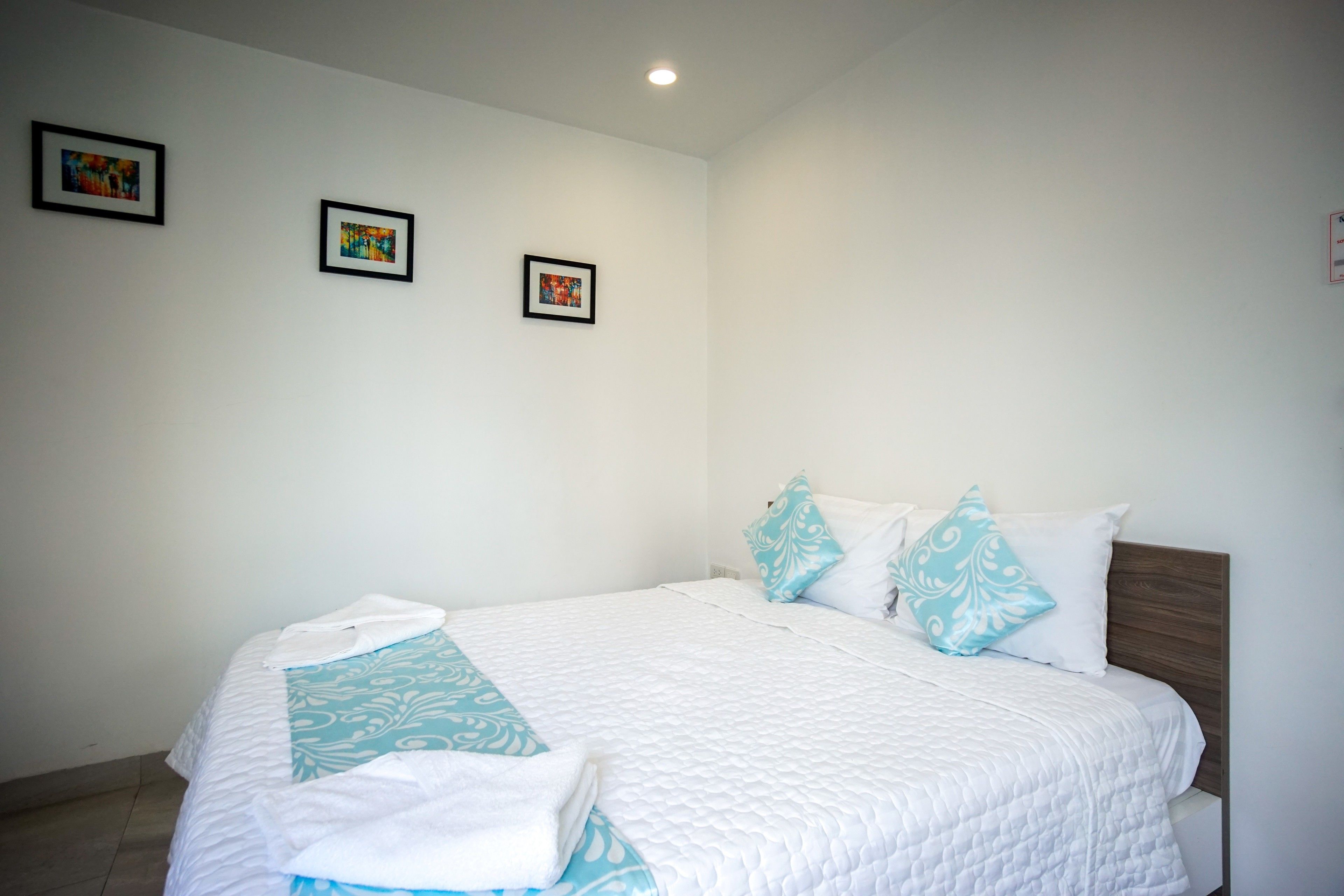 A neatly made bed with a white quilt and blue accents, a wooden headboard, and three framed pictures on the wall.